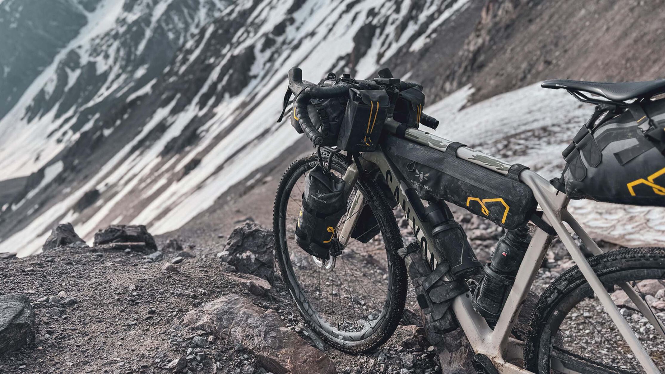 Close-up of a Canyon bikepacking setup in a snowy alpine environment, with frame bags, handlebar packs, and lighting gear prepared for extreme terrain and long-distance adventure.